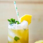 Chilled pineapple ginger mojito in a tall glass and garnished with fresh mint and a wedge of pineapple.