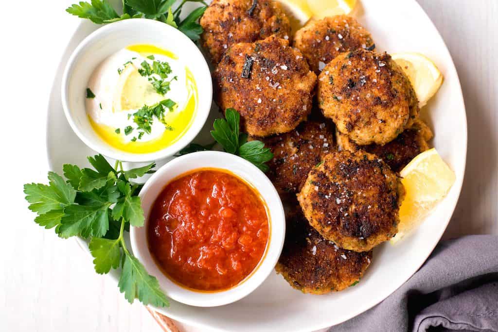 Mediterranean Fish Cakes full of bright lemon zest, garlic, leeks and spices and served along side smoky cumin tomato sauce and lemon horseradish to dip into.