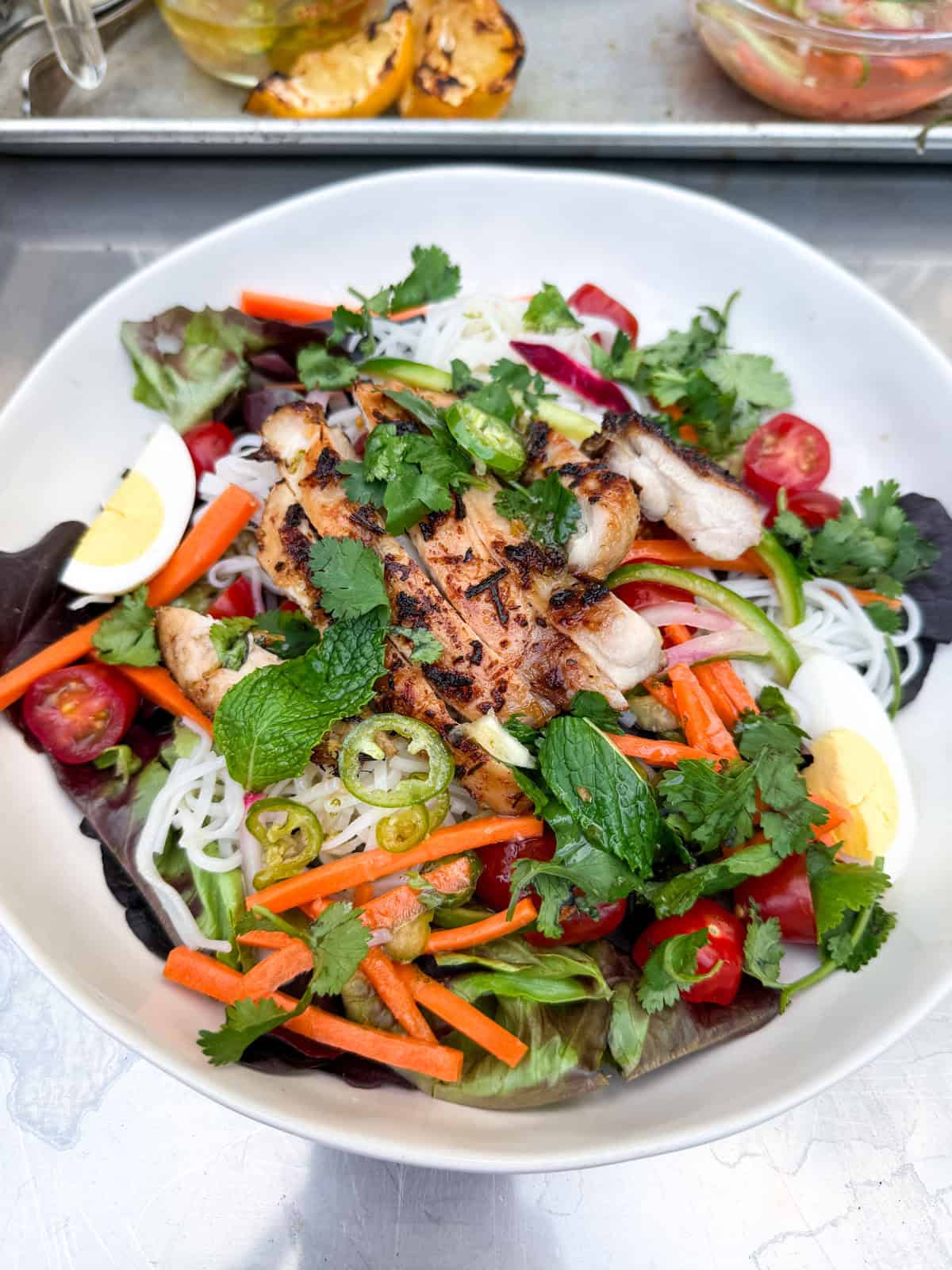 Assemble the rice noodle salad with th4e salad greens, rice noodles, grilled chicken, pickled veggies and egg. 