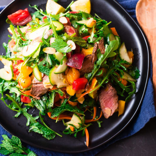 Thai steak salad with fresh herbs of mint and basil and colorful vegetables of peppers and cucumbers.