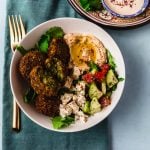 A flavorful and colorful falafel bowl filled with fresh greens, Israeli chopped salad, homemade falafel and finished with a creamy tahini yogurt sauce.