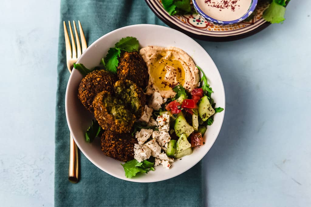 A flavorful and colorful falafel bowl filled with fresh greens, Israeli chopped salad, homemade falafel and finished with a creamy tahini yogurt sauce. 