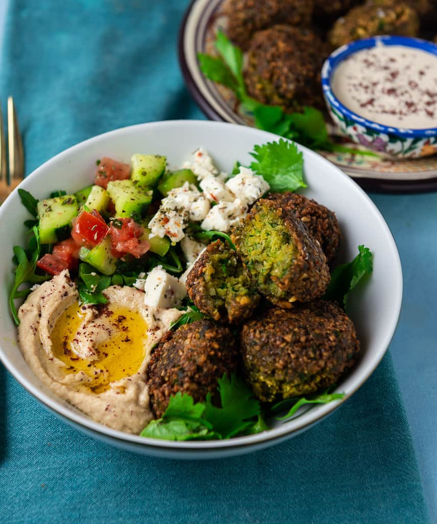 Fried falafel balls served in a bowl with chopped salad and hummus. 