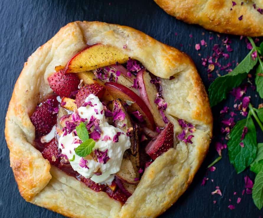 This easy strawberry galette is filled with peaches, berries and scented with a touch of rose water. Then topped with homemade whipped cream.