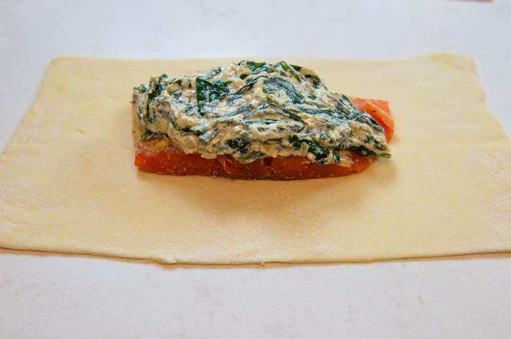 Unbaked salmon wellington with a filet of salmon centered on top of thawed puff pastry and layered with a creamy spinach mixture.