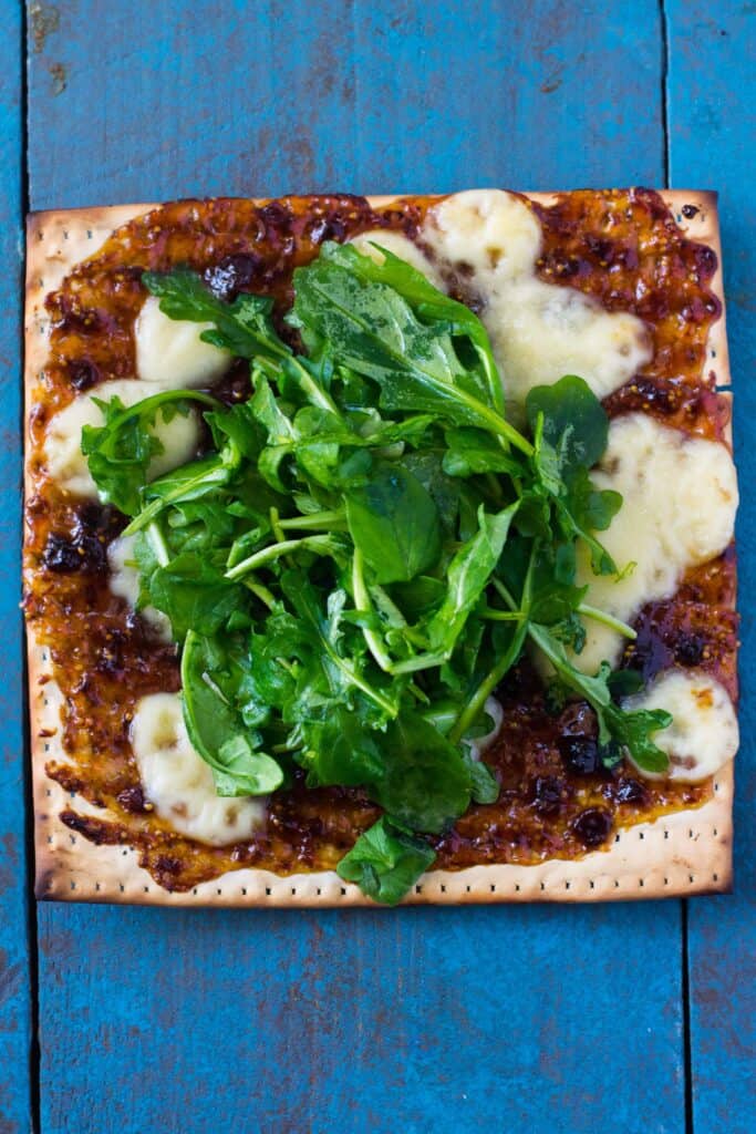 French inspired matzo topping with fig jam, crie cheese and topped with arugula that is dressed with olive oil and lemon juice.