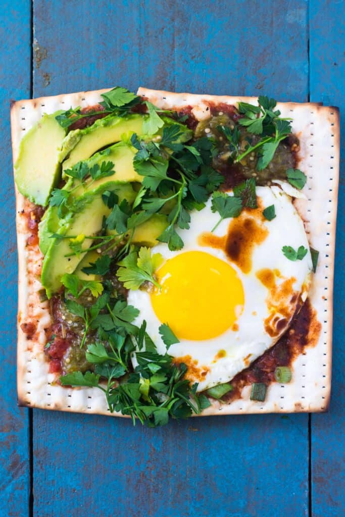 Mexican inspired matzo pizza is a play on huevos rancheros, one of our all time favorite breakfasts! Roasted tomatillo salsa is spread onto the matzo and topped with a perfectly fried egg, cilantro and of course, extra hot sauce. 
