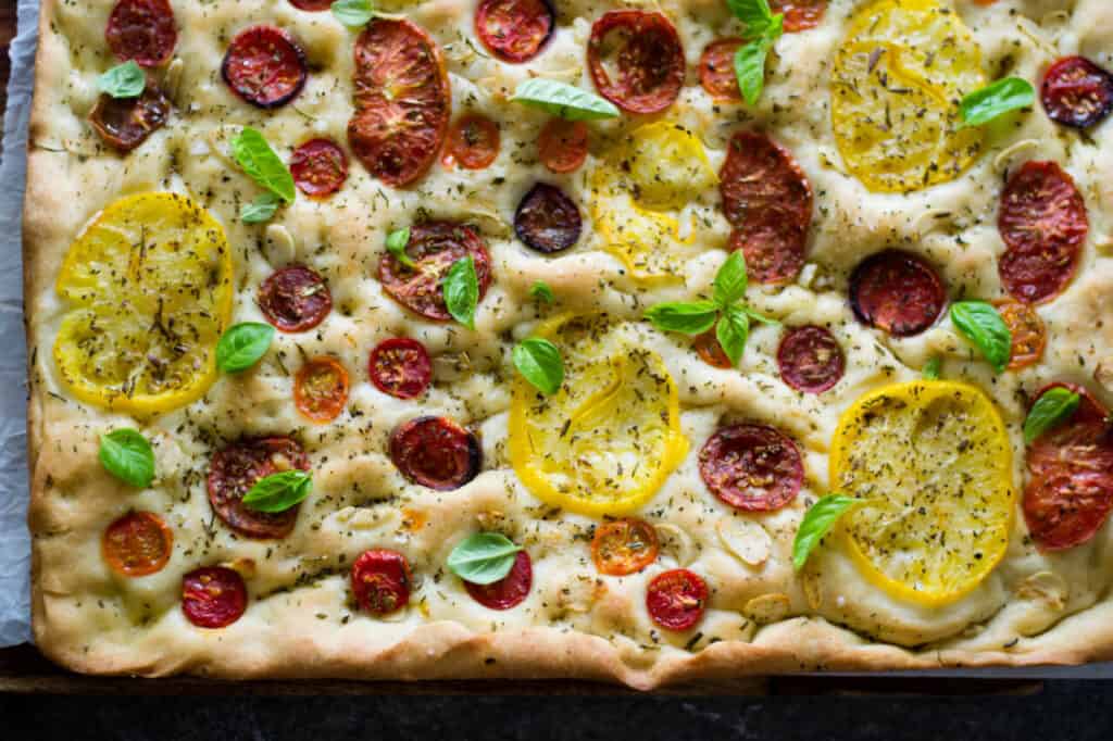 Heirloom tomato and garlic focaccia has slices of tomatoes and garlic nestled into savory focaccia bread with loads of fresh herbs.