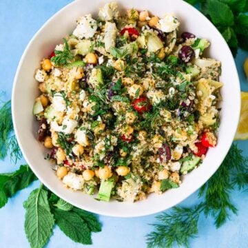 Greek quinoa salad with chickpeas, cherry tomatoes, chopped cucumbers, artichoke hearts, olives and cubes of feta cheese. The quinoa salad is tossed with a lemon vinaigrette and fresh mint and fresh dill.