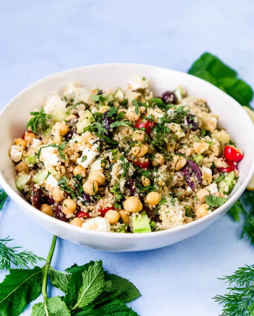 Greek quinoa salad with chickpeas, cherry tomatoes, chopped cucumbers, artichoke hearts, olives and cubes of feta cheese. The quinoa salad is tossed with a lemon vinaigrette and fresh mint and fresh dill.