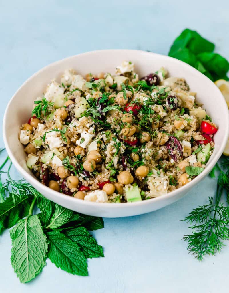 Greek quinoa salad with chickpeas, cherry tomatoes, chopped cucumbers, artichoke hearts, olives and cubes of feta cheese. The quinoa salad is tossed with a lemon vinaigrette and fresh mint and fresh dill.