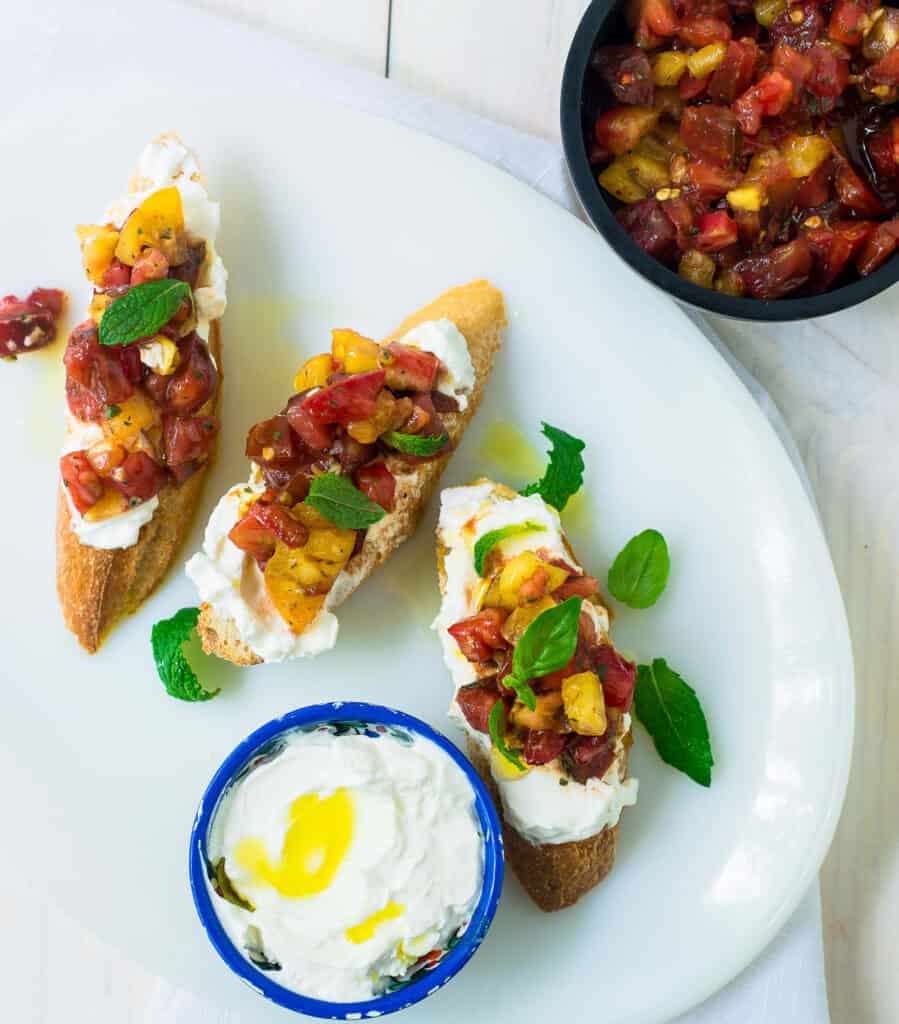 This heirloom tomato bruschetta has a bit of a Middle Eastern twist. Colorful heirloom tomatoes are tossed with balsamic, Aleppo pepper and fresh mint and generously topped onto crostini that is spread with creamy labneh cheese.