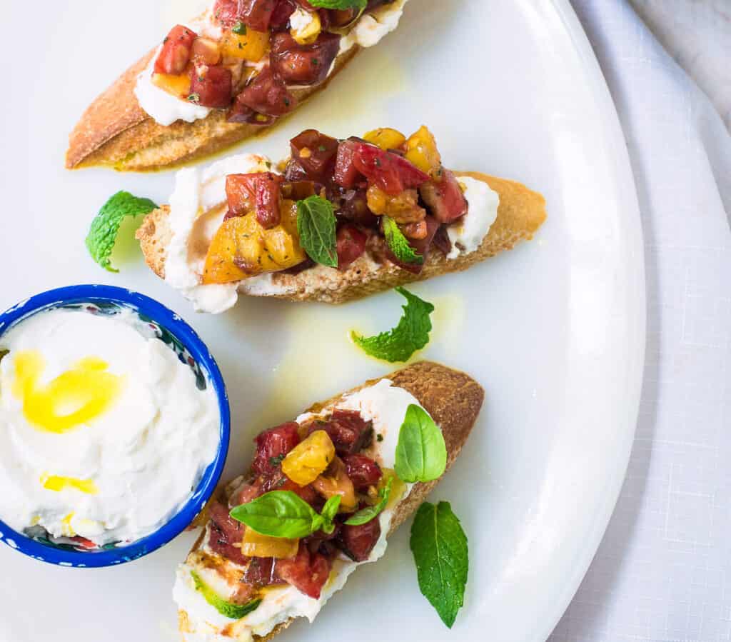 This heirloom tomato bruschetta has a bit of a Middle Eastern twist. Colorful heirloom tomatoes are tossed with balsamic, Aleppo pepper and fresh mint and generously topped onto crostini that is spread with creamy labneh cheese.