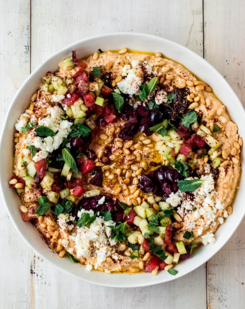This loaded hummus is generously garnished with all the toppings including chopped salad, crumbled feta cheese, toasted pine nuts, olive oil, olives and bold spices. 