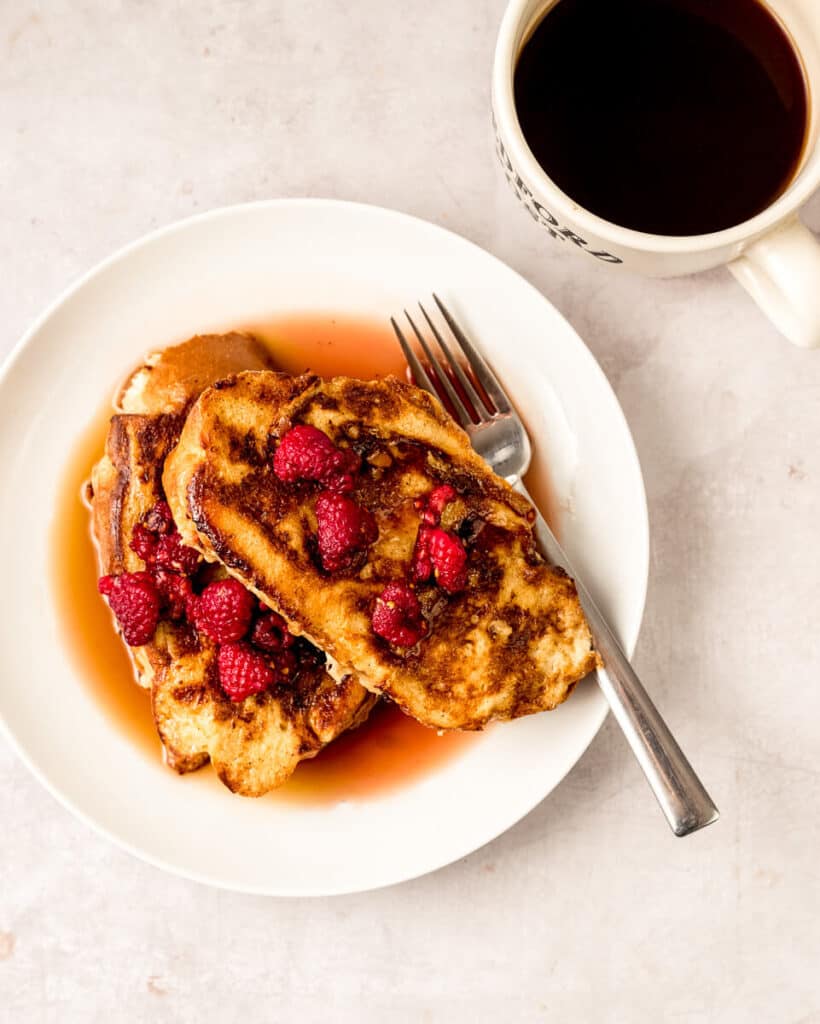 Challah French toast is pan fried to golden brown and served with a warm raspberry maple syrup that has been poured over the French toast.