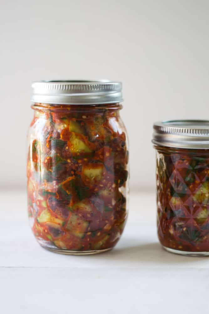 Prepared cucumber kimchi is packed into glass mason jars. The cucumber kimchi is flavored with Korean red pepper, ginger, garlic, green onion and sesame oil. 