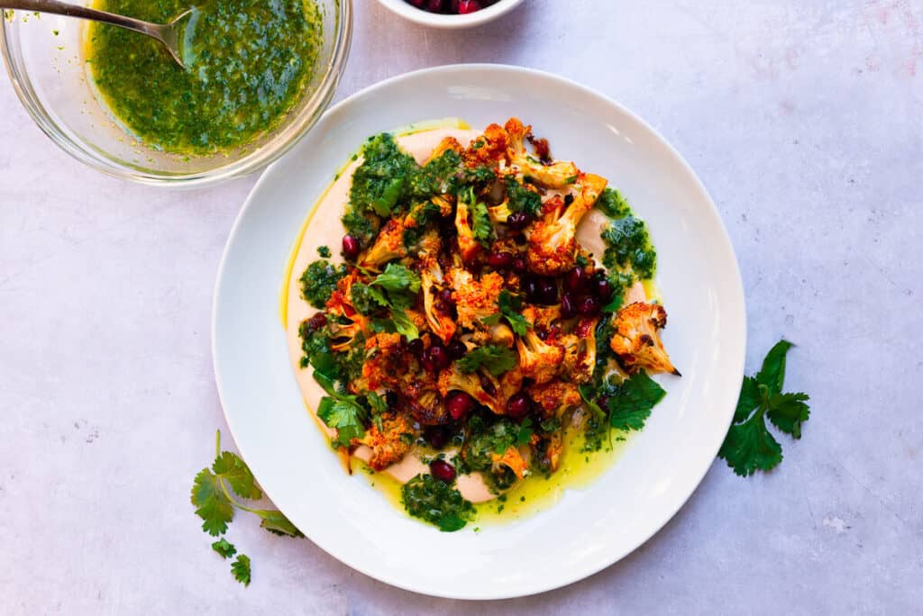 Honey harissa roasted cauliflower is layered on top of creamy harissa tahini and finished with a bright cilantro vinaigrette and sweet pomegranate seeds.