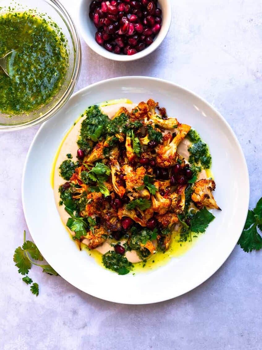 Honey harissa roasted cauliflower is layered on top of creamy harissa tahini and finished with a bright cilantro vinaigrette and sweet pomegranate seeds.