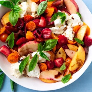 This colorful summer fruit caprese salad is arranged in a wide bowl and is full of sliced peaches and nectarines, quartered strawberries and sweet orange cherry tomatoes. The caprese salad is topped with roughly torn fresh mozzarella cheese, basil leaves and a good drizzle of extra virgin olive oil and vinegar.