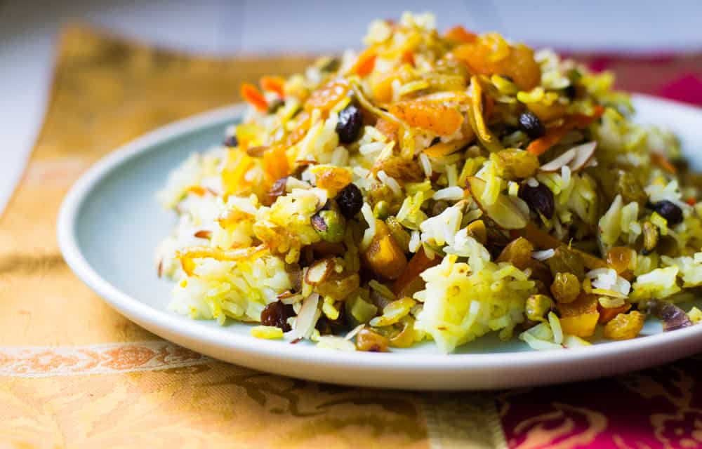 Colorful jeweled Persian rice is piled high on a wide platter. The persian rice is studded with dried apricots, pistachios, slivered almonds and candied orange peel. 