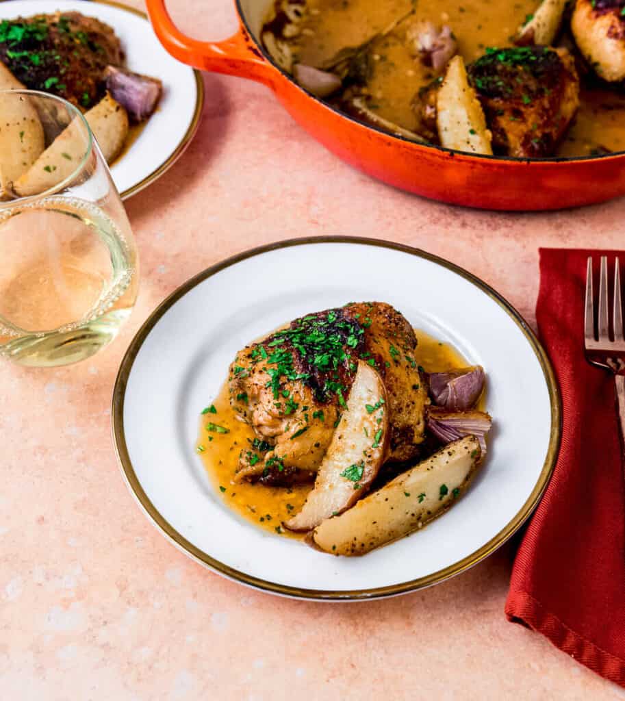 Honey Dijon glazed chicken thighs are roasted with wedges of pears and shallots until the chicken skin is caramelized. The chicken is garnished with chopped parsley and served with a glass of white wine. 
