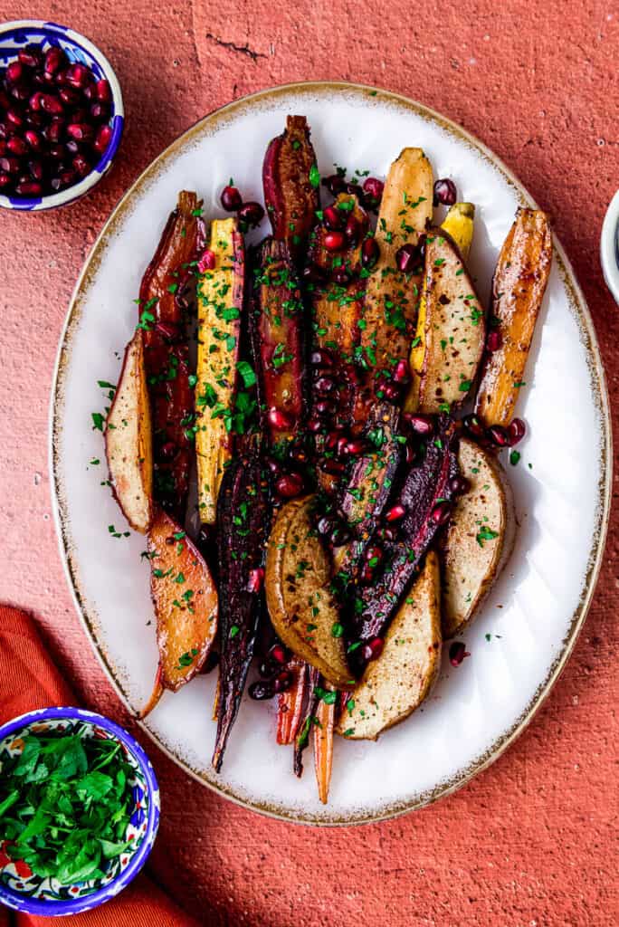Rainbow carrots and red anjou pears flavored with pomegranate molasses and maple syrup and are roasted until just caramelized. The carrots and pears are arranged on an oval platter and topped with pomegranate seeds and fresh chopped parsley. 