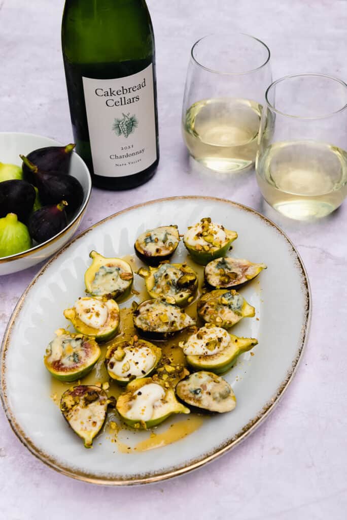 Baked fresh figs are topped with blue cheese and goat cheese, chopped pistachios and drizzled with honey. The baked figs are paired with Chardonnay wine.