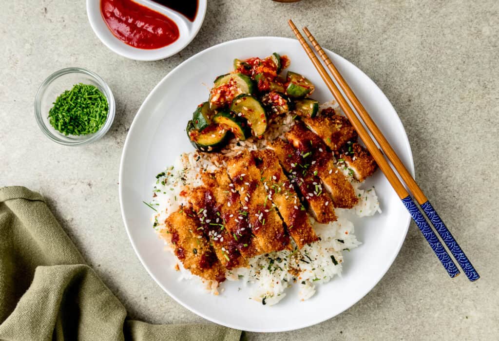 Hawaii style chicken katsu is a fried chicken cutlet that's been coated with panko bread crumbs and furikake. Once fried, the chicken is served on top of cooked white rice and katsu sauce drizzled on top and cucumber kimchi on the side. 