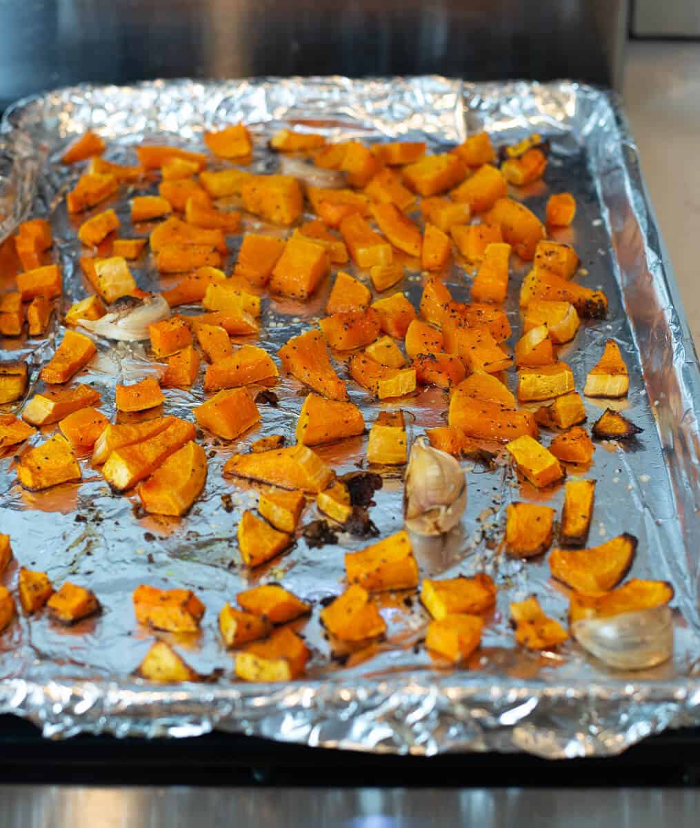 Roasted cubes of butternut squash with whole cloves of garlic on a sheet pan.