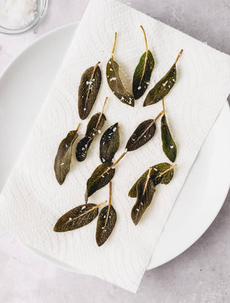 Crisp fried sage leaves on a plate and sprinkled with flakey salt.