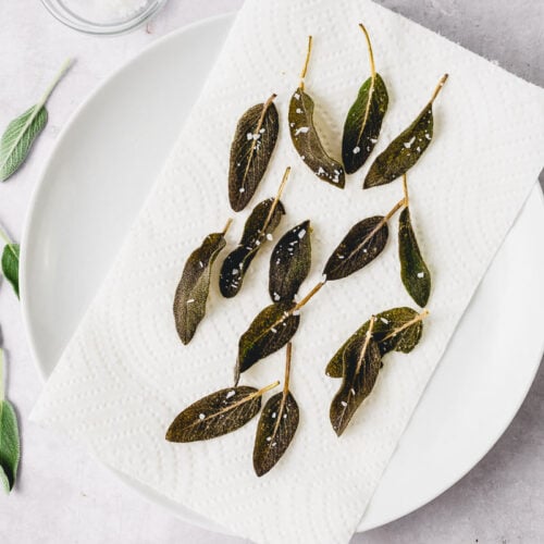 Crisp fried sage leaves are scattered on a plate and sprinkled with salt.