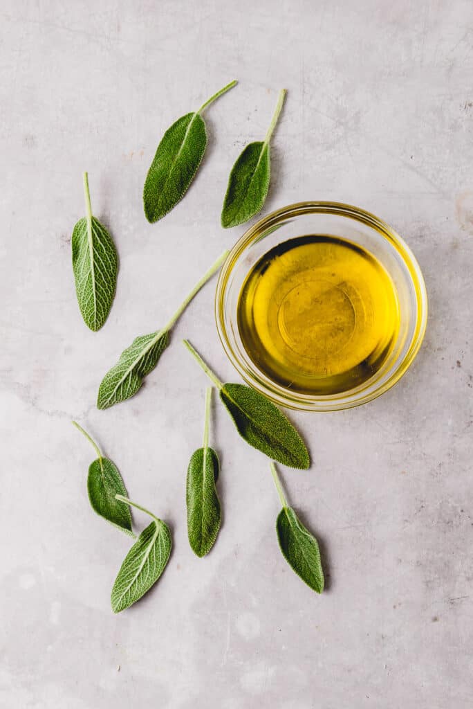 Fresh sage leaves with a bowl of olive oil.