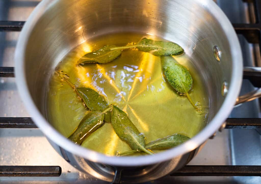 A handful of fresh sage leaves are frying in a small pot with oil.