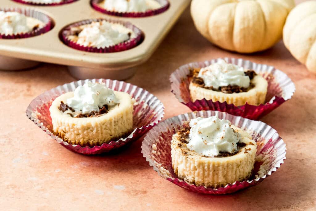 Mini cheesecakes have a swirl of pumpkin in the mixture and topped with a dollop of whipped cream. 