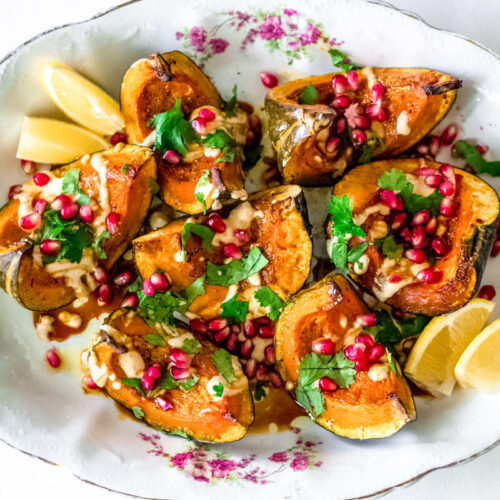 Acorn squash is drizzled with tahini and topped with chopped parsley and pomegranate seeds.