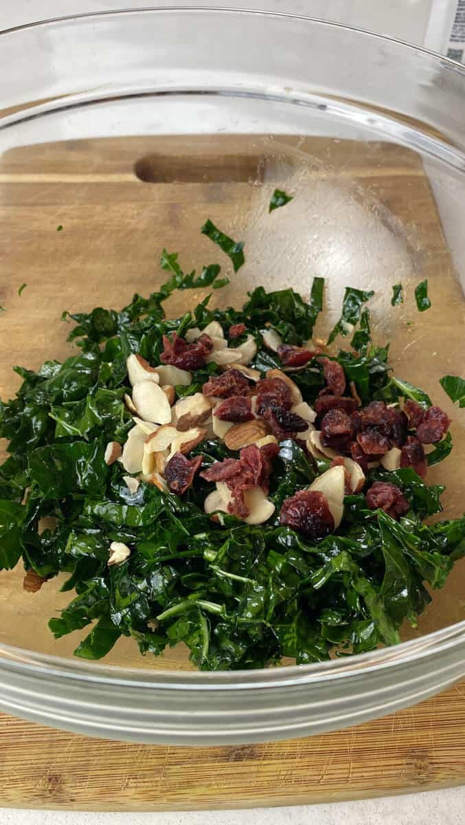 Add dried cranberries to kale and apple salad in a bowl.