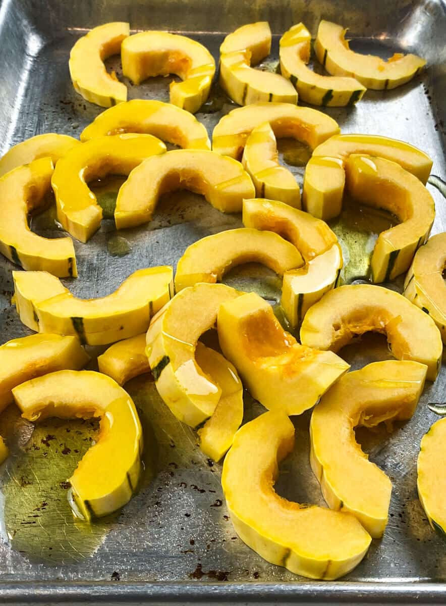 Lay prepped delicata squash onto a baking sheet and drizzle with olive oil.