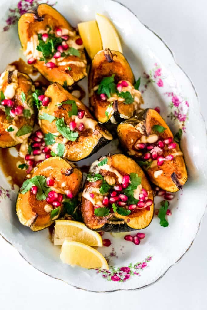 Roasted acorn squash is quartered and laid out on a platter and drizzled with tahini and topped with pomegranate and fresh herbs.