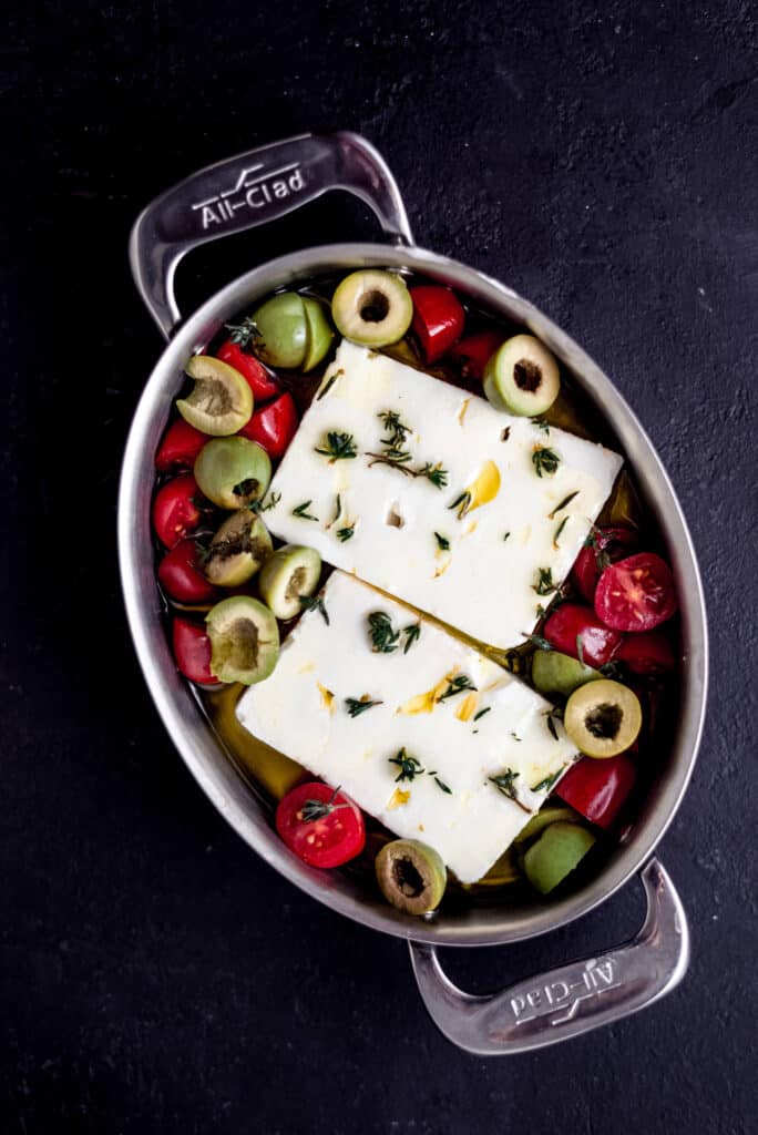 Place block of feta in a small baking dish and drizzle with olive oil, fresh thyme, cherry tomatoes and olives.