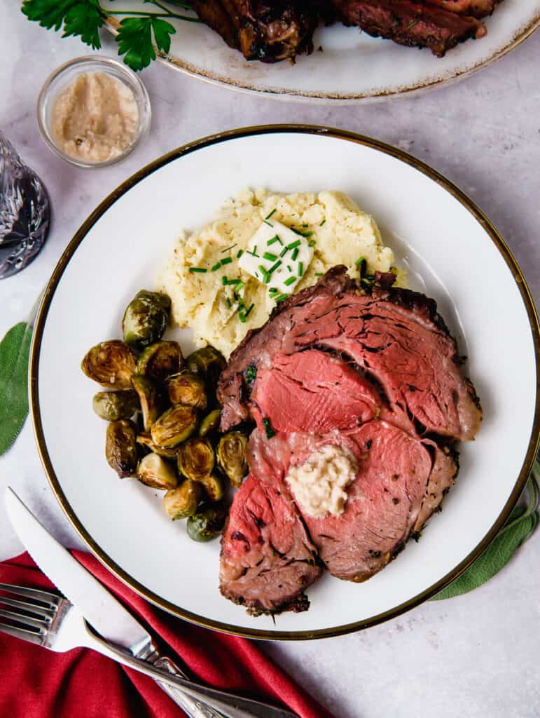Boneless rib roast sliced on a plate with a dollop of horseradish and mashed potatoes.