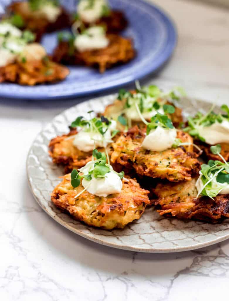 Crispy potato latkes are on a plate and topped with dollop of sour cream and microgreens.