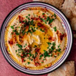Easy and creamy homemade hummus is garnished with olive oil and sprinkle of paprika on top.