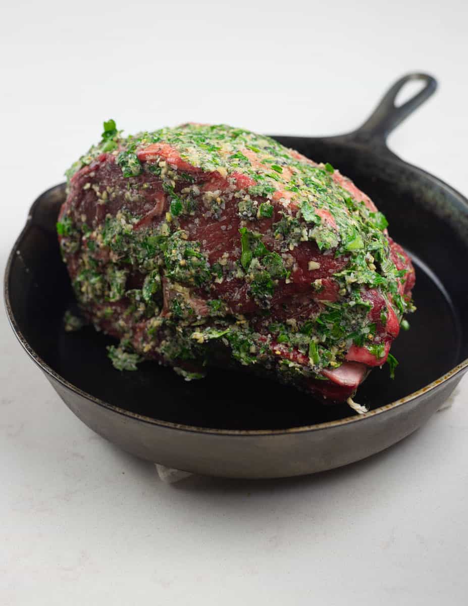 Rub the herb compound butter onto the boneless rib roast and place inside a cast iron skillet.