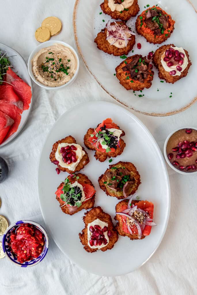 Plated fried latkes with assorted toppings, such as guacamole, brisket and Calabrian chiles.