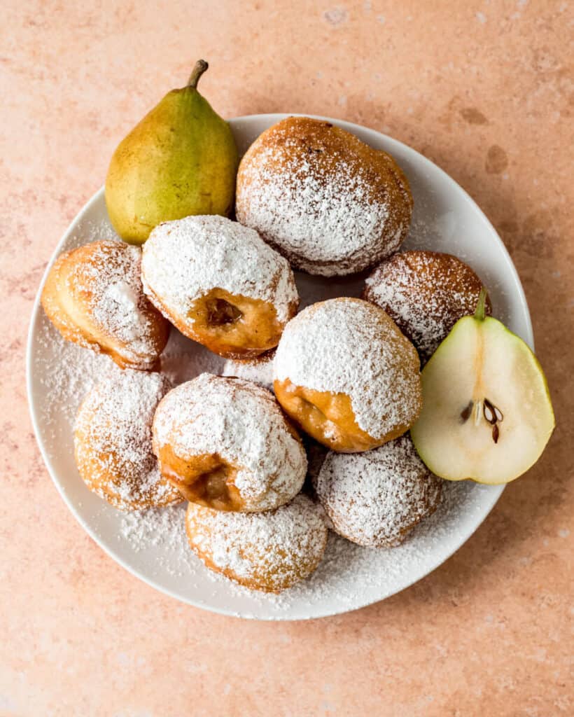 Pear donuts are piled on a plate and dusted with powdered sugar.