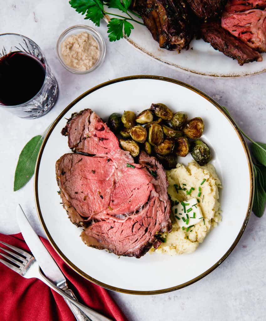 Sliced boneless rib roast with mashed potatoes and roasted brussels sprouts.