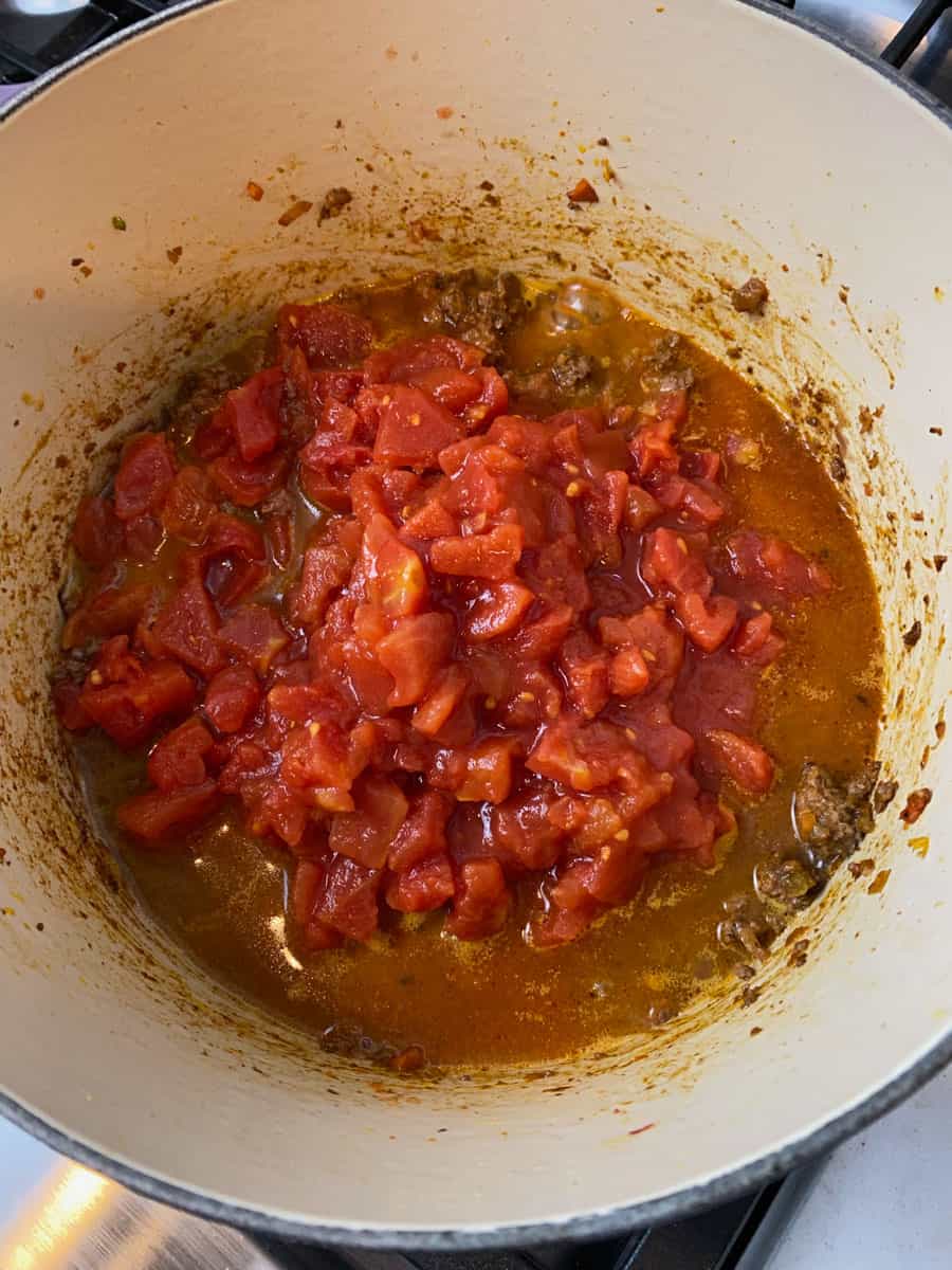 Add canned chopped tomatoes to the bolognese mixture.