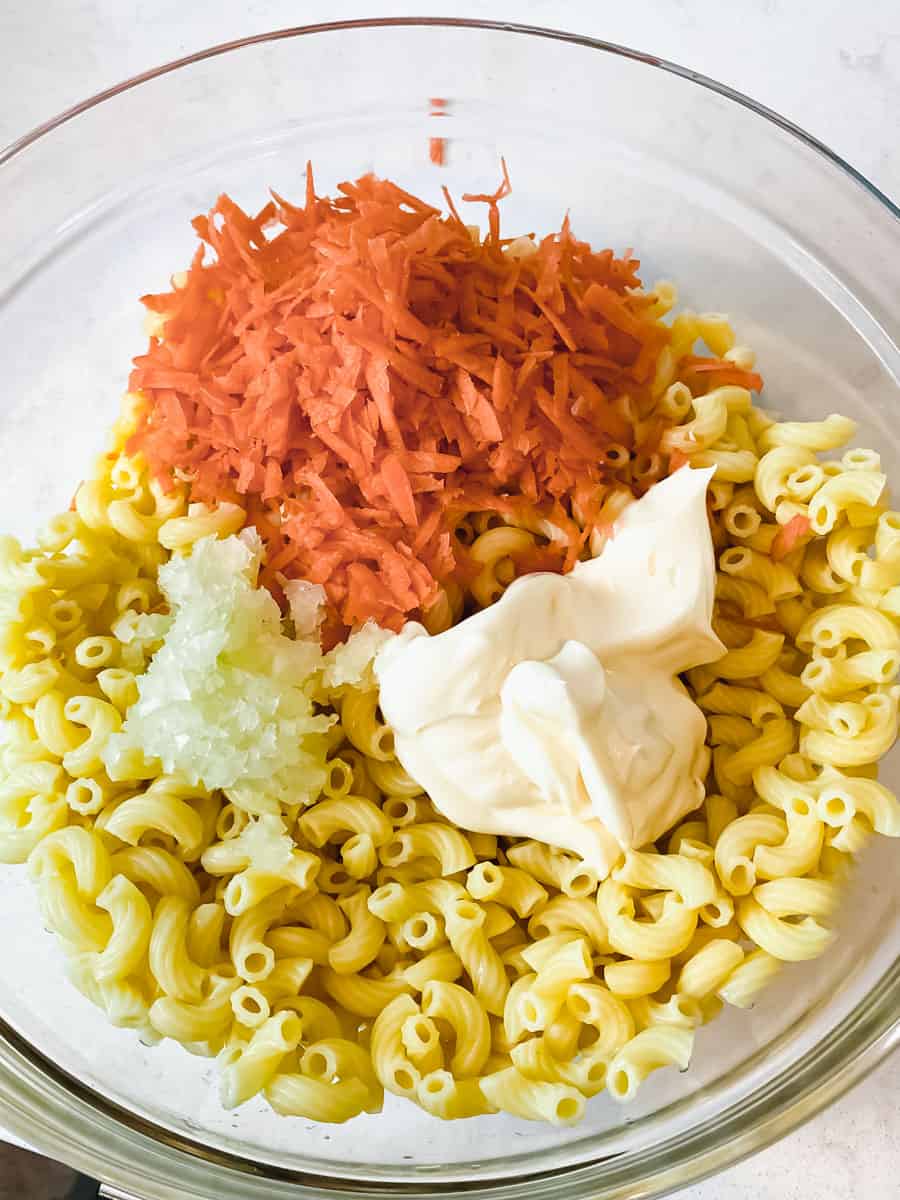 To the cooked macaroni noodles, add Best Foods mayo, grated carrot, grated onion and a bit of sugar.