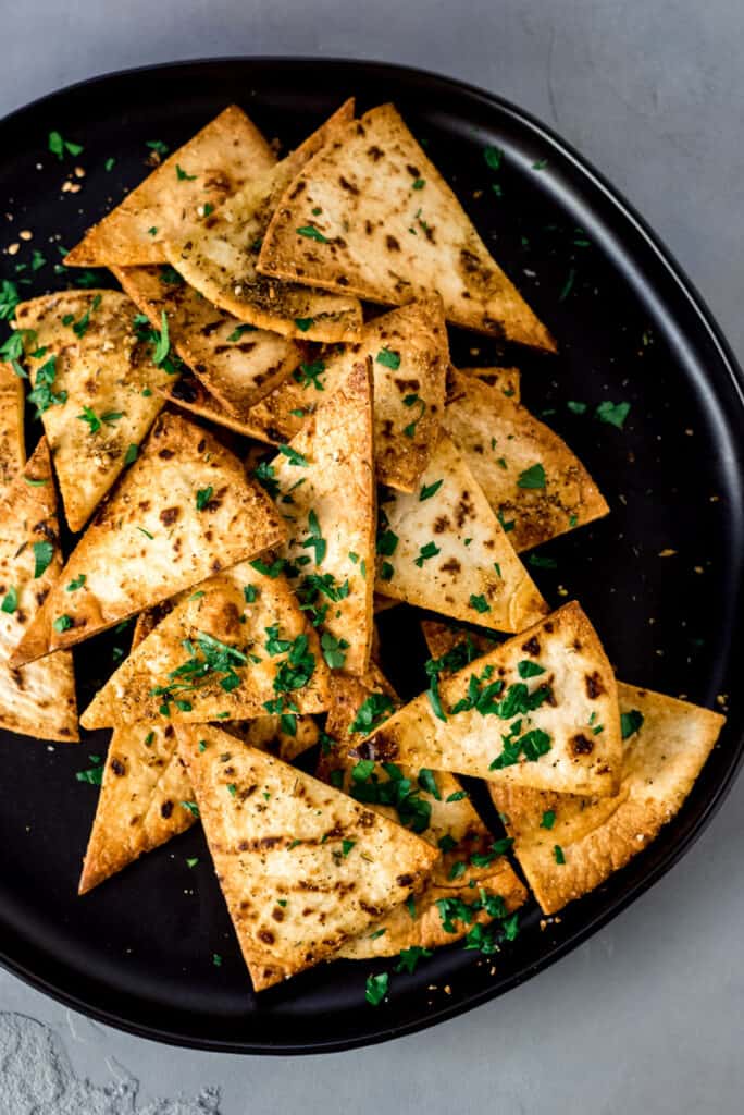 Homemade pita chips scattered onto a plate and garnished with chopped parsley.