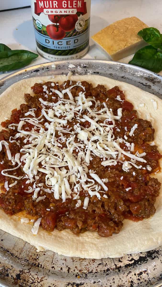 Top the bolognese pizza with shredded mozzarella cheese.